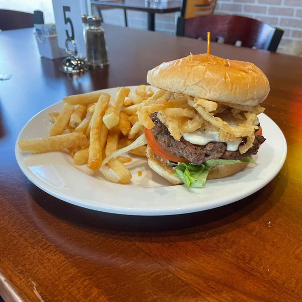 A burger with crispy onion rings, lettuce, tomato, and fries on a white plate at ONEWAY Cafe and Pizza.