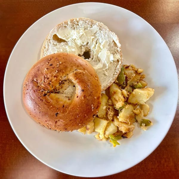 Everything bagel with cream cheese and a side of home fries with green peppers on a white plate.