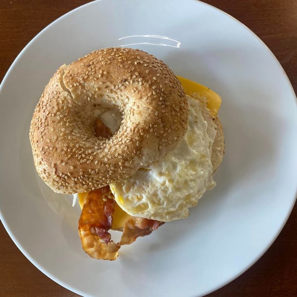 A sesame seed bagel with fried egg, bacon, and cheese on a white plate.