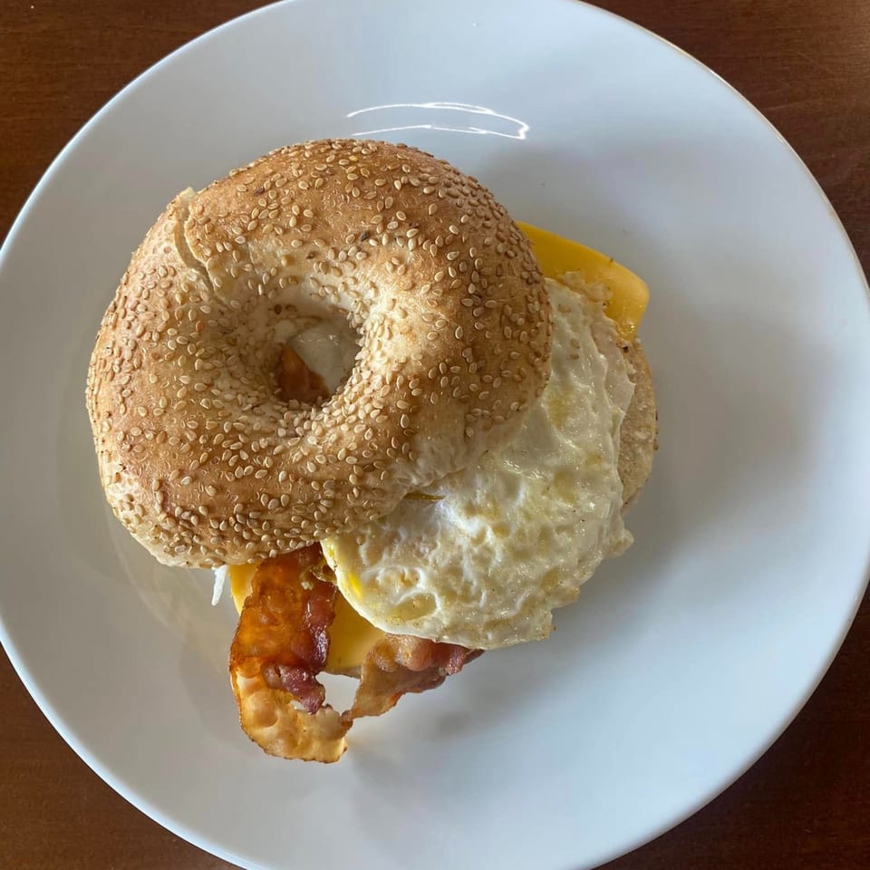A sesame seed bagel with fried egg, bacon, and cheese on a white plate.