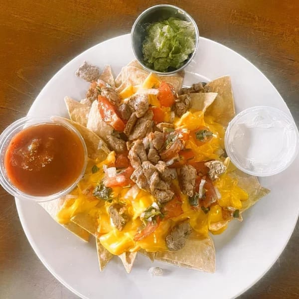 A plate of nachos with melted cheese, meat, diced tomatoes, and onions, served with salsa and guacamole.